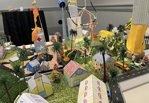 Colorful miniature city layout with houses, trees, roads, and decorative lights, created during a City Build team building activity.