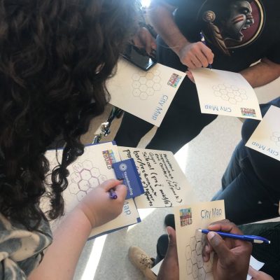 Team members collaborating on city maps at a City Build team building event, sketching ideas and planning zones for their project. thumbnail