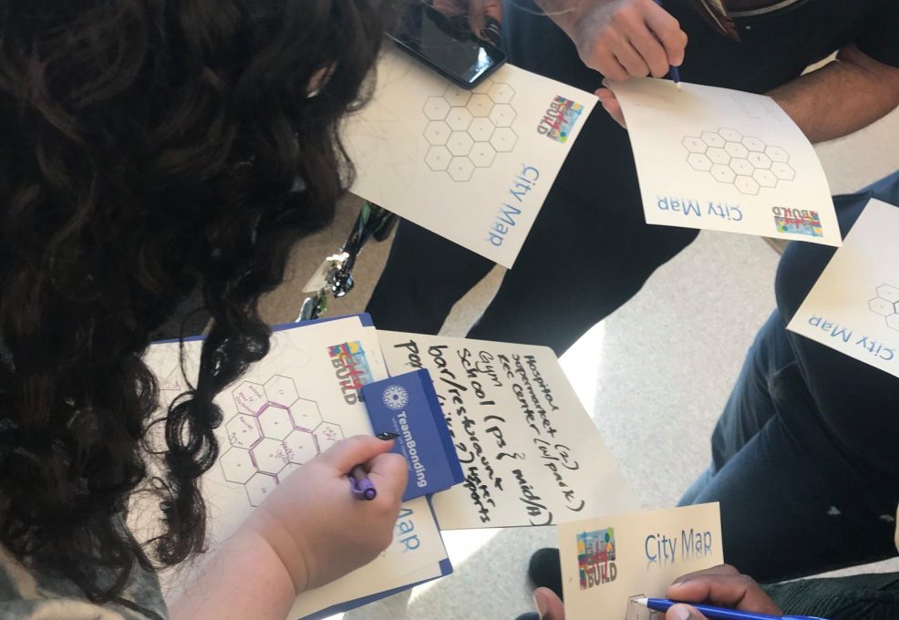 Team members collaborating on city maps at a City Build team building event, sketching ideas and planning zones for their project.