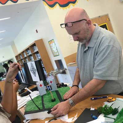 A participant carefully works on a miniature urban zone during a City Build team building event, focusing on adding details to the landscape. thumbnail