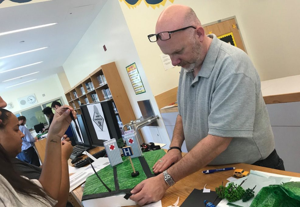 A participant carefully works on a miniature urban zone during a City Build team building event, focusing on adding details to the landscape.