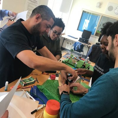 Team members collaborate on a City Build team building activity, constructing miniature urban landscapes using green materials and small props. thumbnail