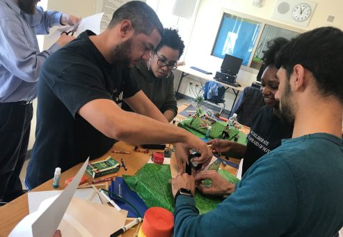 Team members collaborate on a City Build team building activity, constructing miniature urban landscapes using green materials and small props.