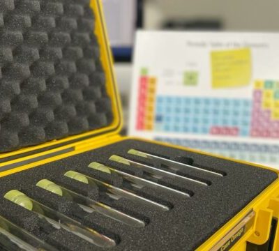 Close-up of a yellow case holding test tubes, with a periodic table in the background, used as part of the 'Atmosphere' team building event. thumbnail