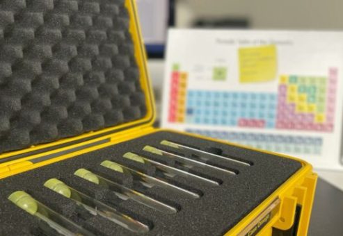 Close-up of a yellow case holding test tubes, with a periodic table in the background, used as part of the 'Atmosphere' team building event.