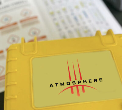 Close-up of a yellow case labeled 'Atmosphere' used in a team building activity, with instruction sheets visible in the background. thumbnail