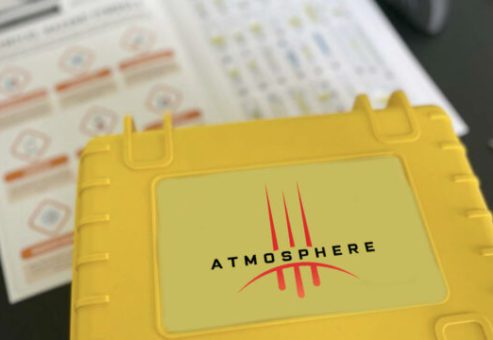 Close-up of a yellow case labeled 'Atmosphere' used in a team building activity, with instruction sheets visible in the background.
