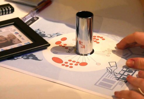 Participant solving a puzzle by using a reflective cylinder on a diagram during the 'Atmosphere' team building event.