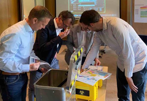 Group of participants analyzing documents and tools around a biohazard-themed box as part of the 'Atmosphere ' team building activity.