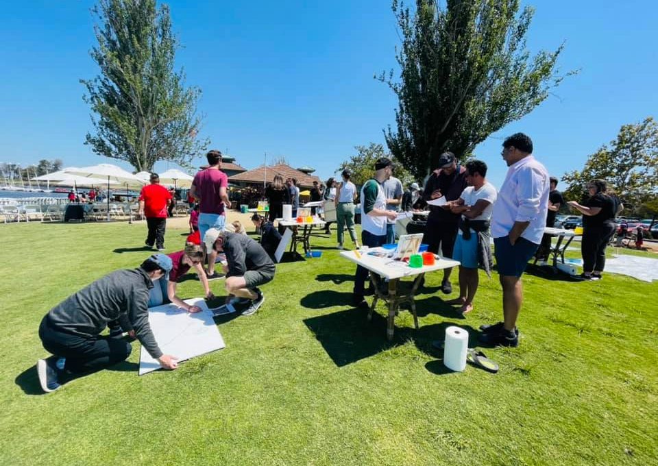 Teams collaborate outdoors on individual canvases during The Big Picture team building event, working together to create a collective mural that promotes communication and teamwork.