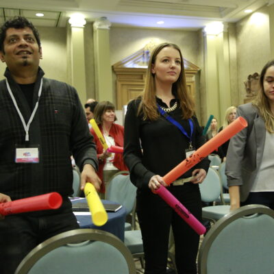 Participants standing and playing colorful Boomwhackers in sync during a musical team building activity, fostering teamwork and coordination. thumbnail