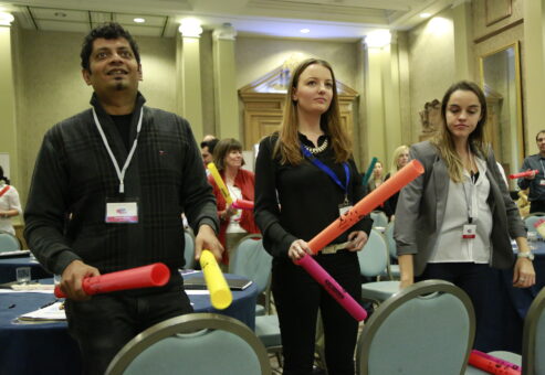 Participants standing and playing colorful Boomwhackers in sync during a musical team building activity, fostering teamwork and coordination.