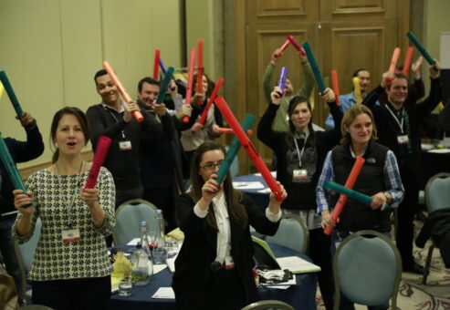 Participants enthusiastically hold colorful Boomwhackers during a high-energy Boom Time team building activity, fostering teamwork and rhythm-based collaboration.