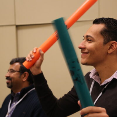 Two participants smiling and playing colorful Boomwhackers during a fun, music-based team building activity, enhancing teamwork and rhythm skills. thumbnail