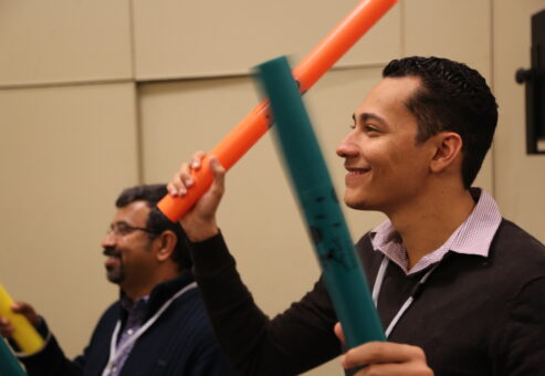 Two participants smiling and playing colorful Boomwhackers during a fun, music-based team building activity, enhancing teamwork and rhythm skills.