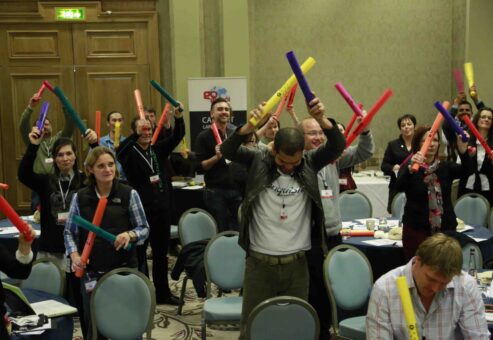 Group of participants enthusiastically playing colorful Boomwhackers in unison during a dynamic team building activity, fostering collaboration and rhythm.
