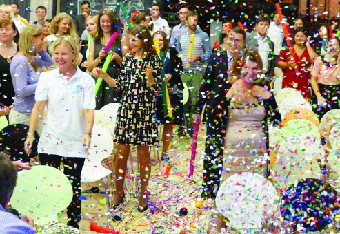 Team participating in Boom Time, a musical team building activity. Participants are surrounded by confetti and colorful Boomwhackers, collaborating to create music and enhance teamwork, energy, and communication.