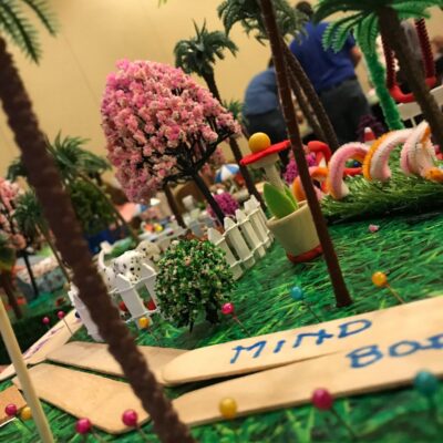 Close-up of a creative miniature city build with vibrant greenery, pink trees, and decorative pathways during a City Build team building event. thumbnail