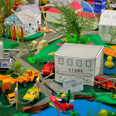 Close-up of a colorful miniature city created during the City Build team building event, featuring small buildings, toy vehicles, and greenery. thumbnail