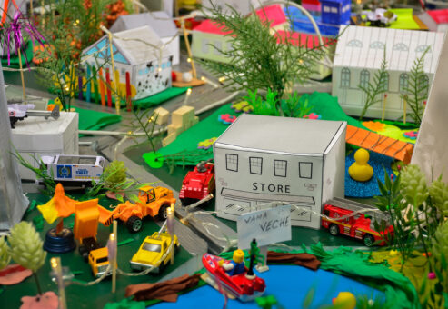 Close-up of a colorful miniature city created during the City Build team building event, featuring small buildings, toy vehicles, and greenery.