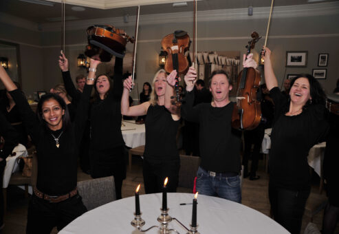 Excited participants raise their violins triumphantly after performing together during the Crescendo team building event.