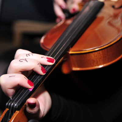 A close-up of a participant's hand learning violin finger placement during a Crescendo team building event, with numbers written on their fingers for guidance. thumbnail