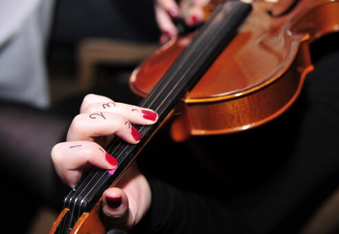 A close-up of a participant's hand learning violin finger placement during a Crescendo team building event, with numbers written on their fingers for guidance.
