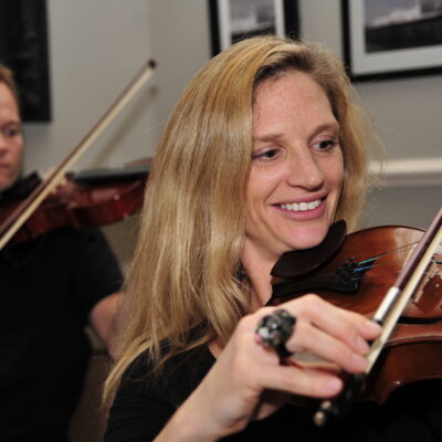 Smiling participants learning to play violins together during the Crescendo team building event, highlighting teamwork and musical collaboration. thumbnail