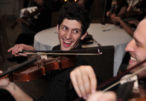 Two participants laughing and playing violins during the Crescendo team building event, creating music together in a joyful atmosphere.