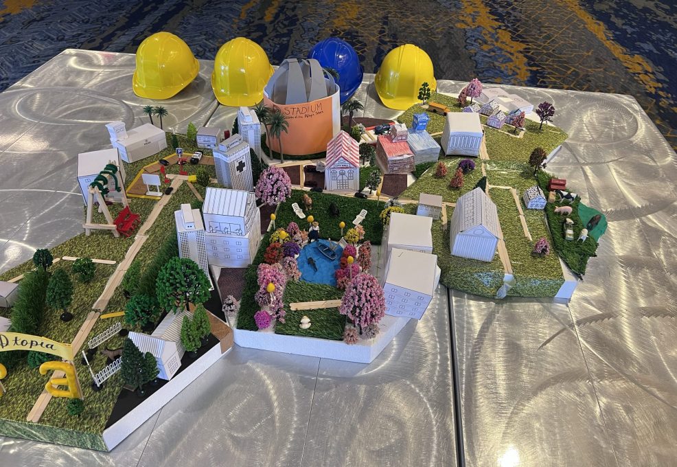 Close-up of a completed miniature city model at the City Build team building event, surrounded by yellow and blue hard hats, showcasing teamwork and creativity.