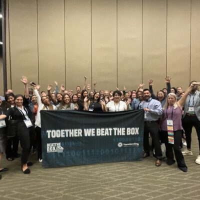 Large group of participants proudly displaying the 'Together We Beat The Box' banner after successfully completing a collaborative team building event. thumbnail