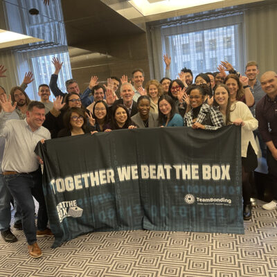 A large group of excited participants celebrate their victory after successfully completing the Beat The Box team building challenge, proudly displaying their teamwork banner. thumbnail
