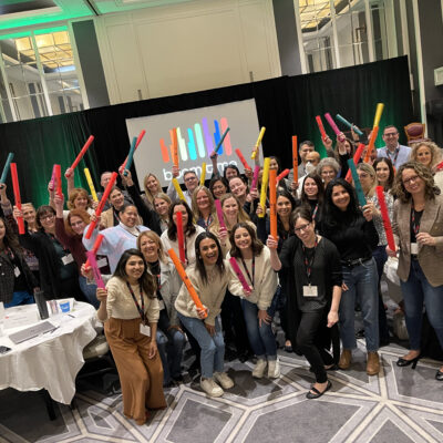 A group of participants at a Boom Time team building event hold colorful Boomwhackers above their heads, smiling and posing together. thumbnail