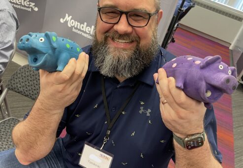 Man smiling and holding two colorful percussion instruments shaped like hippos during a BeatsWork team building activity.