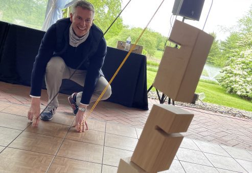 A participant smiling while carefully adjusting a stack of wooden blocks during the Integrity team building event, focusing on precision and collaboration.