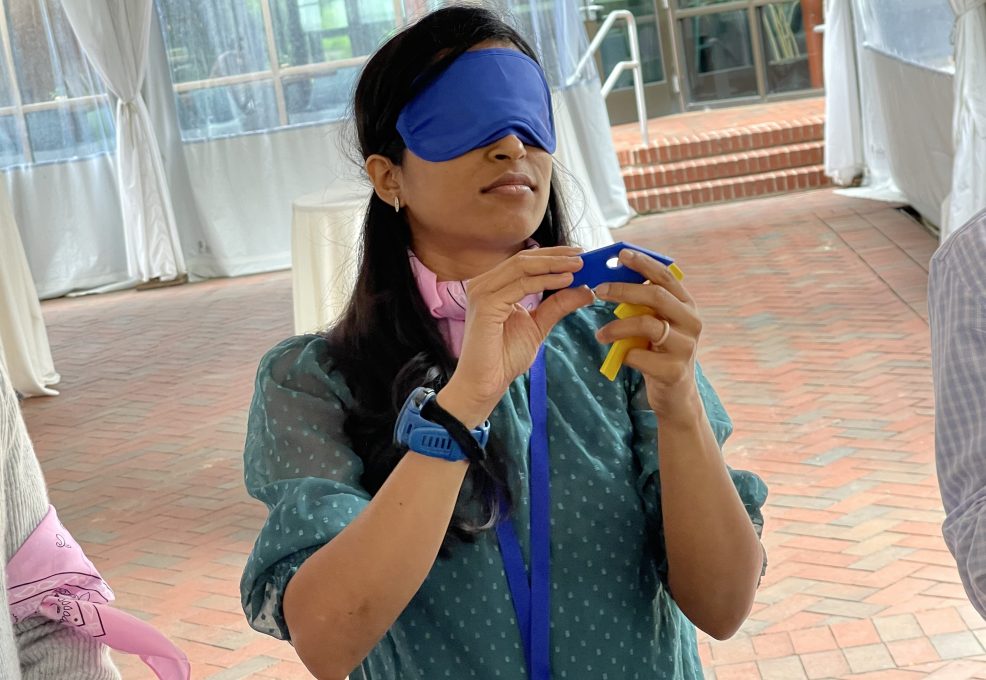 A participant in the Integrity team building event, blindfolded and carefully handling a challenge item, demonstrating focus and teamwork.