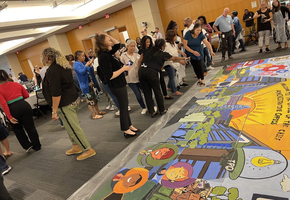 Participants gather to assemble their completed canvases into a large mural during The Big Picture team building event, showcasing their collaborative artwork and teamwork efforts.