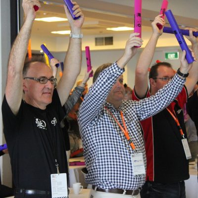 Team members participating in Boom Time, raising their Boomwhackers to play music together. This team building activity encourages collaboration, rhythm, and teamwork, creating an engaging and energetic atmosphere. thumbnail