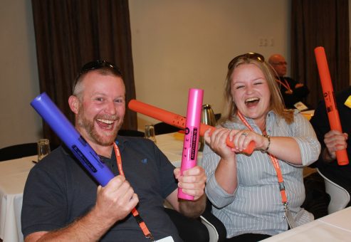 Team members smiling and laughing while participating in Boom Time, a musical team building activity. They use colorful Boomwhackers to create music, enhancing collaboration and boosting team spirit.