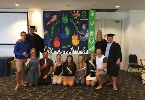 A group of participants proudly posing in front of their completed mural, created during The Big Picture team building event. The mural features words like 
