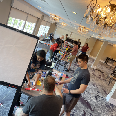 Teams working together in a spacious room, building creative contraptions during the Domino Effect team building event. thumbnail