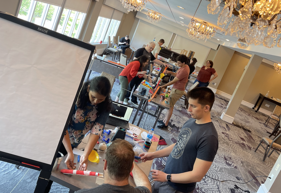 Teams working together in a spacious room, building creative contraptions during the Domino Effect team building event.