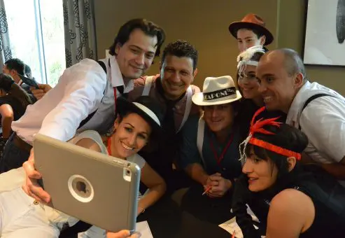 A team dressed in 1920s gangster-themed outfits gathers for a selfie during the high-energy Escape the Mob team building event, solving clues and creating their alibi.