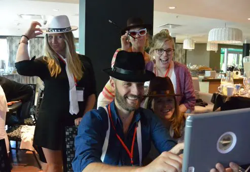 A team dressed in fun hats and posing for a photo during the Escape the Mob team building event, combining creativity and teamwork to solve the mystery.