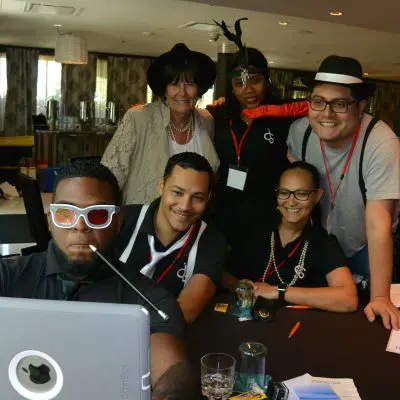 A team strikes a fun pose with an iPad during the Escape the Mob team building event, working together to solve the team building challenge. thumbnail