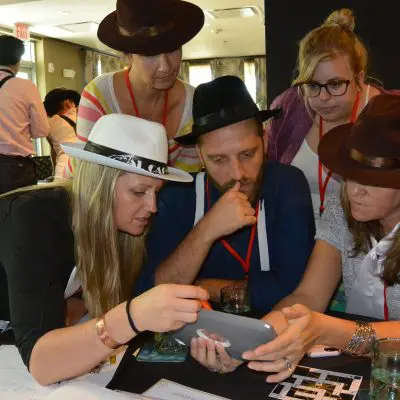 A focused team in the Escape the Mob team building challenge works together using an iPad to solve clues and establish their alibi in this high-energy mystery event. thumbnail