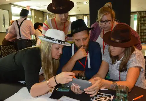 A focused team in the Escape the Mob team building challenge works together using an iPad to solve clues and establish their alibi in this high-energy mystery event.