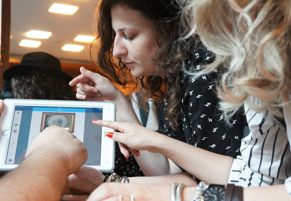 Three people closely examining a clue on a tablet screen during the 'Escape the Mob' team building activity. They are focused and engaged in solving a mystery, collaborating to piece together information and create a strategy for the game.