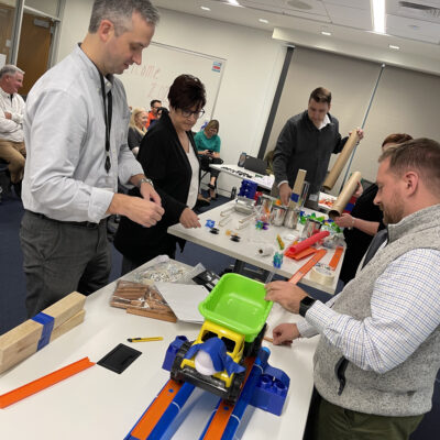 Participants engaged in the Domino Effect team building event, assembling creative contraptions using colorful materials. thumbnail