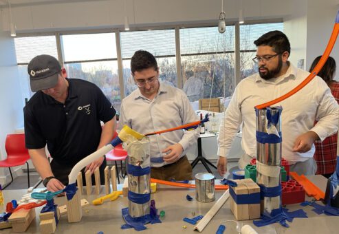 Team members collaborating to construct a creative machine in the Domino Effect team building event.